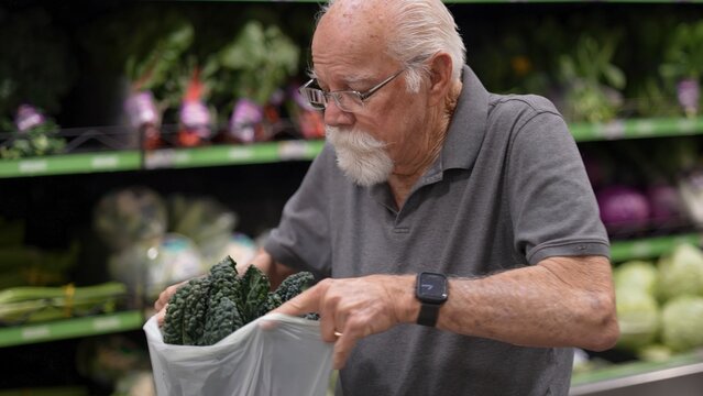 An elderly man is in a grocery store checking the contents of his bag filled with vegetables. He is focused on his shopping