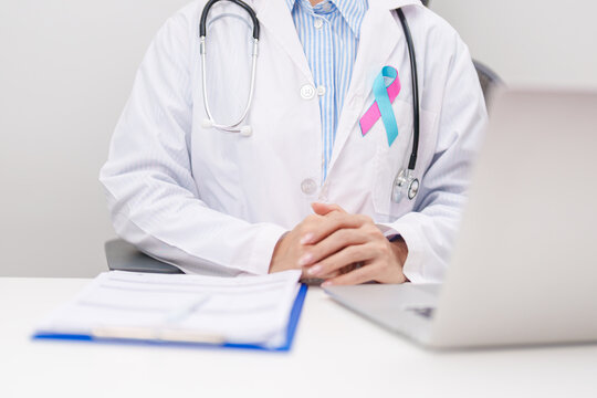 doctor using laptop and report notes on notebook. blue and pink ribbon concept of October male Breast Cancer Awareness month, National Cancer Survivors Month and Pink October Healthcare