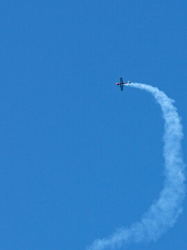 Aerobatic Stunt Plane Performing Maneuvers with Smoke Trail in Blue Sky