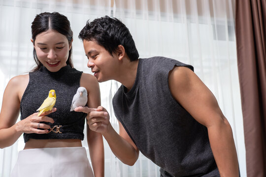 Couple playing with pet, tiny forpus bird indoors.