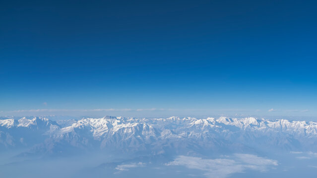 Beautiful mountain landscape. View from a height, from an airplane. Snow-capped peaks of the majestic Himalayas against the blue sky. There is fog and haze in the valley. Nepal.