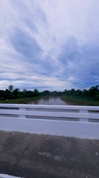 Scenic View of a River and Lush Greenery Under a Dramatic Cloudy Sky from a Bridge Perspective