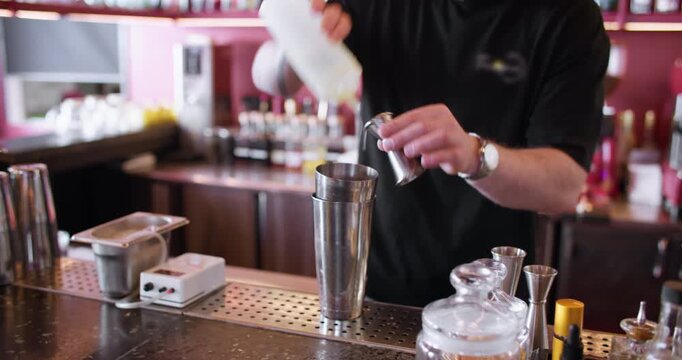 Cocktail recipe. Measuring ingredient. Bartender pouring white liquid for chilled flavor drink from squeezer jigger to cold shaker.