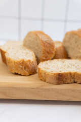 Fototapeta premium Fresh bread slices rest on a wooden board. Golden crusts contrast with soft, airy interiors. White tiles form a clean. Ideal for food blogs, recipe covers