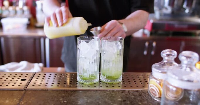 Cocktail recipe. Bartender service. Man hand measuring syrup pouring aroma liquid for chilled drink from metal jigger to ice glass.