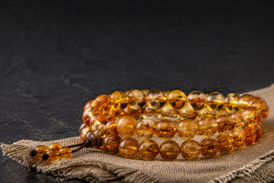 Honey-colored resin bead bracelet on linen cloth, organic plant inclusions, dark slate background, amber tones, jewelry presentation