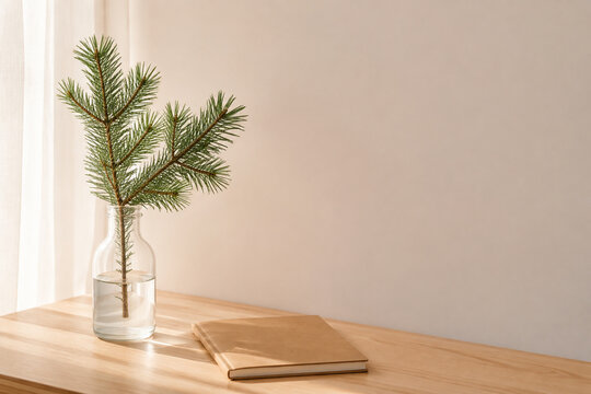 Pine branch in glass bottle vase on wooden desk next to blank notebook, simple workspace and nature concept