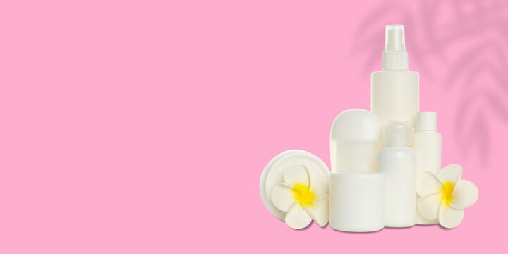 Cosmetics. Variety of cosmetic containers arranged with tropical flowers on pink background