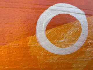 Close up macro view of a painted decorative mural on a building exterior featuring bold orange and white geometric circle patterns in Leucadia, California. © Bryan Lambert