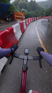 A cyclist rides on a wet mountain road, surrounded by safety barriers and traffic cones, capturing the thrill of cycling in rainy conditions.