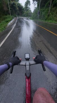 Cyclist Riding on Wet Road During Rainy Day with Lush Greenery and Curved Pathway in Scenic Outdoor Adventure