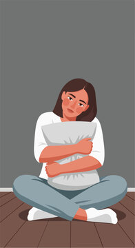 Woman hugging pillow on floor, looking sad, against grey wall