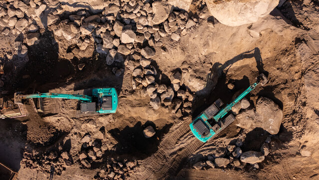 Aerial view of an excavator working in a deep dirt pit with rocky terrain and shadows cast on the ground in Indonesia