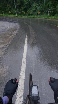 A cyclist rides on a wet, winding mountain road surrounded by lush greenery, showcasing adventure and nature.