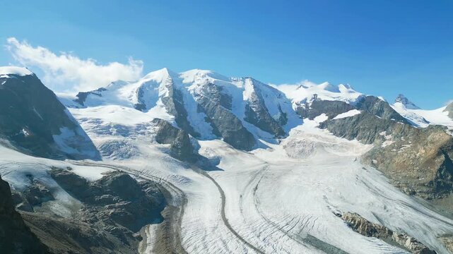Aerial view of Piz Palu and the Pers Glacier with snow-capped peaks, rocky ridges, and deep crevasses under a clear blue sky in Pontresina, Graubunden, Switzerland.