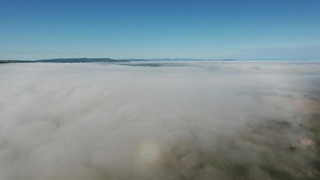 Aerial view of thick morning fog blanketing the rolling hills of the Tuscan countryside in Pienza, Tuscany, Italy.