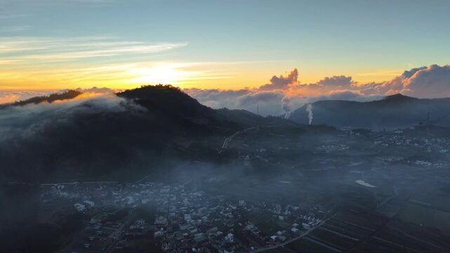 Aerial view of Dieng Plateau at sunrise with volcanic mist, rolling hills, and a small village nestled in the valley in Indonesia.