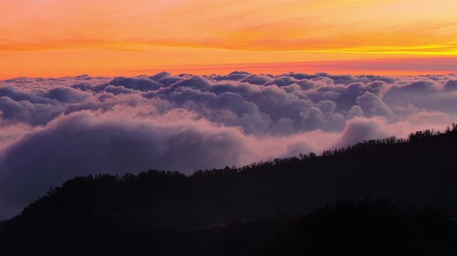 Aerial view of Dieng Plateau with thick clouds blanketing the mountainous landscape during a vibrant sunset in Indonesia.