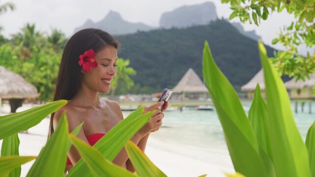 Asian beauty woman using phone in bikini on tropical beach. Beautiful young woman on vacation and travel using smartphone app. Raw unedited video of real woman model without any makeup