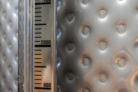 Close up of 2000 and 900 markings on a measurement scale of a stainless steel wine tank, showing liquid volume monitoring equipment used in winery and beverage production.
