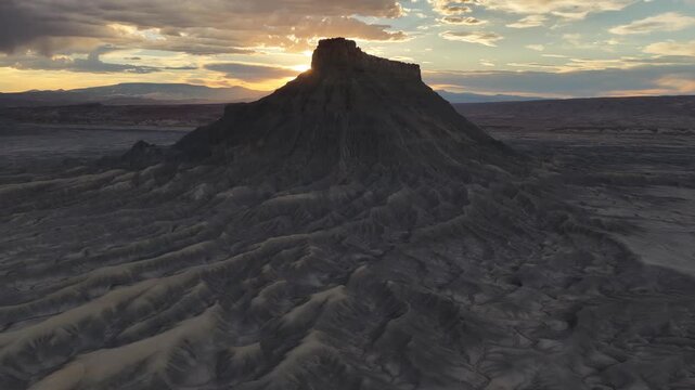 Aerial view of Factory Butte rising above the rugged, eroded badlands of the desert landscape at sunset in Wayne County, Utah, United States.