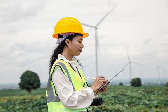 Engineer using a digital tablet at a green wind turbine farm to inspect renewable energy operations.