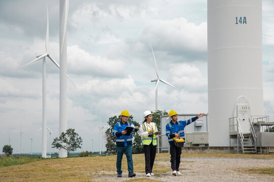 Team of engineers in hard hats walking through a wind turbine farm to perform maintenance and site inspections.