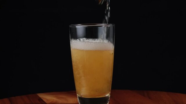 Closeup hoppy unfiltered beer foaming in glass. Foam alcohol beverage flowing clean goblet on black background. Fresh craft heady liquid bubbling in full transparent mug.