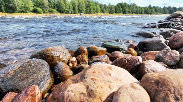Rocky river shoreline with flowing water, gentle waves and moss covered stones, peaceful natural landscape with riverbank texture, outdoor scenery and tranquil wilderness atmosphere