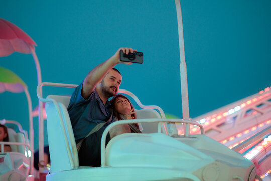 Happy Father Taking Selfie With Daughter On Amusement Park Ride. Smiling dad holding smartphone to capture memories with his young daughter on a carousel
