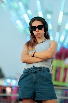 Sulking Stressed Woman With Crossed Arms Wearing Sunglasses in Amusement Park. Anxious or moody girl standing with crossed arms and a funny sulking face at a carnival