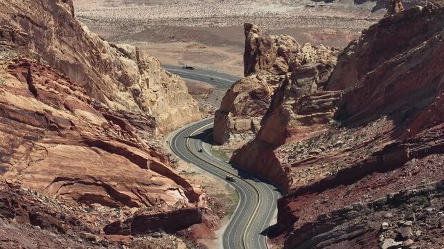 Aerial view of a winding road cutting through the dramatic red rock formations of the San Rafael Reef in Emery County, Utah, United States.