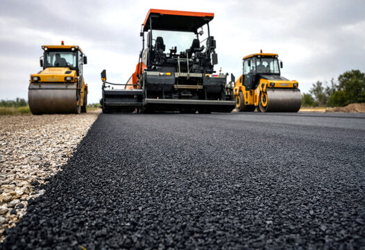 Heavy machinery working on freshly laid asphalt road construction site with road rollers and paver