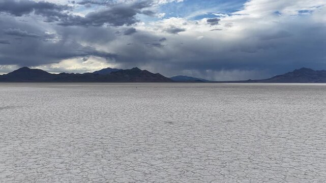 Aerial view of Bonneville Salt Flats with expansive white salt crust and distant mountains under a dramatic cloudy sky, Tooele County, Utah, United States.