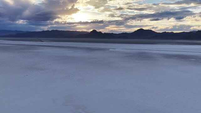 Aerial view of the vast salt crust of the Bonneville Salt Flats under a dramatic sunset sky with distant mountains in Tooele County, Utah, United States.
