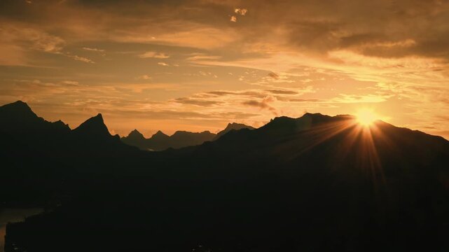 Moorea, French Polynesia, mountains creating dark silhouette against vibrant golden hour orange sunset sky with bright sun rays bursting over the horizon, reflecting sense of peace and natural beauty