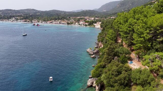 Aerial drone view of rocky green coastline and turquoise sea at Ipsos Bay in Corfu Island, Greece, with boats and yachts