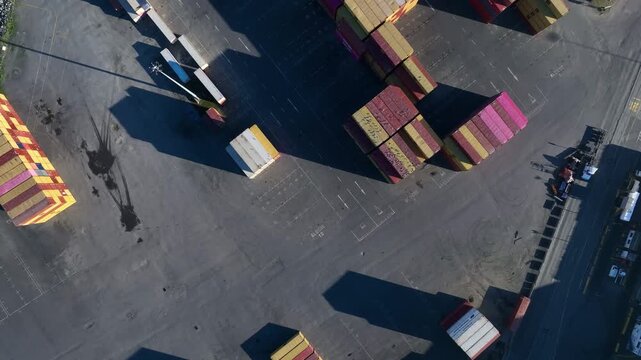 Aerial view of colorful shipping containers stacked in a port area with long shadows cast on the paved ground in Penco, Bio Bio, Chile.