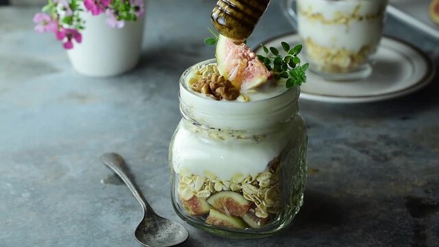Delicious Greek yogurt parfait with fresh figs, oats, and nuts in a glass jar, topped with honey for a healthy breakfast and clean eating concept.