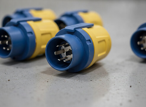Industrial electrical connector close-up, blue and yellow IEC 60309 plug pins, heavy duty power socket, industrial wiring equipment, voltage connection point, technical detail shot