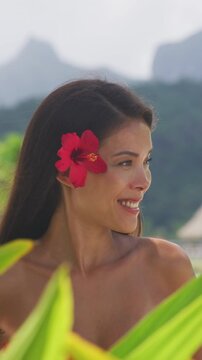 Natural exotic beauty woman in red swimsuit looking serene on tropical beach. Asian bikini model wearing hibicus flower. Body care pampering. Raw vertical video of real woman model without makeup