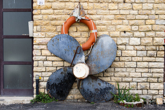 A weathered metal boat propeller and an orange life ring mounted on a rustic stone wall outside a building in Italy creating a charming nautical display