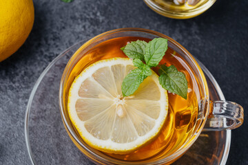 Hot tea with lemon slice and mint leaves in a clear cup on a dark background