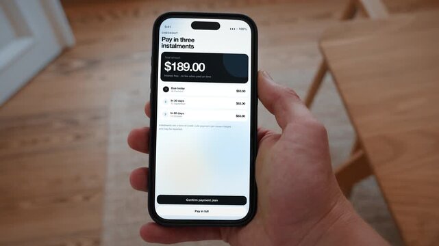 A buy now pay later plan splits the checkout amount into three instalments with the dates shown. Point of view shot with the phone held in the hand. Useful for spreading the cost of a purchase.