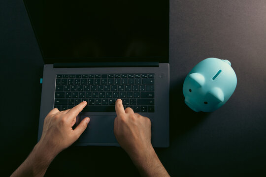 Man using a laptop computer with a blue piggy bank on a black background