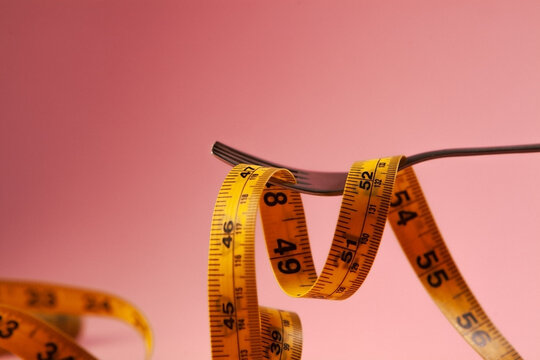 Measuring tape and fork on pink background. Diet and weight loss concept.