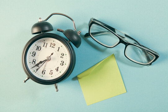 Retro alarm clock, eyeglasses and sticky note on blue background