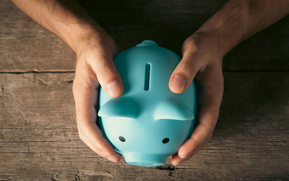 Man holding piggy bank on wooden table, closeup. Money savings