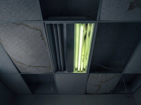 Flickering Fluorescent Light Above Damaged Suspended Ceiling with Water Stains and Exposed Wires