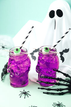 Two purple Halloween drinks in skull glasses with eerie eyeballs and paper bats on a light blue background.